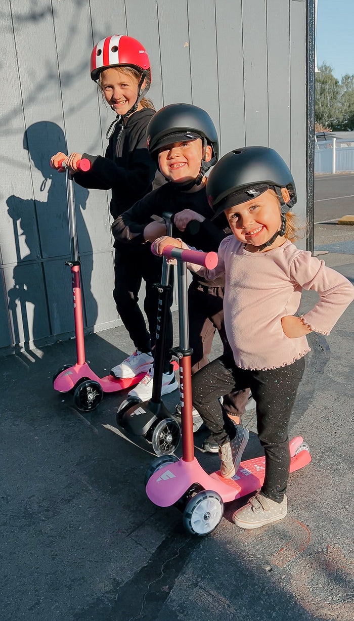 three kids pose with kids scooters
