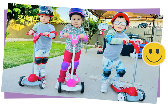 Three children on scooters in a park setting, smiling.