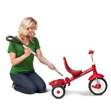 Woman kneeling next to a red tricycle removing the parent push handle on a white background