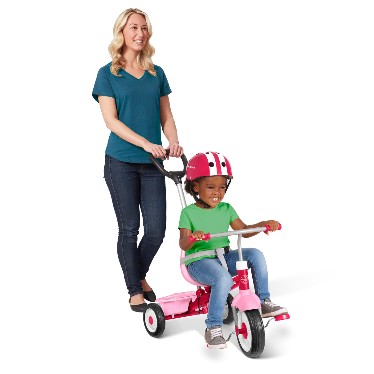 A woman pushes a pink children's tricycle with a seat and handlebar while a young child rides it, wearing a pink and white helmet, against a clean white background.