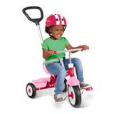 A young child wearing a pink and white helmet sits on a pink and silver push tricycle with a black handlebar, set against a clean white background.