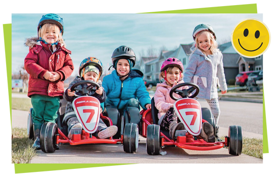 Children in go-karts with helmets on a residential street, smiling.