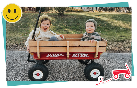 Two children in a red Radio Flyer wagon on a road with a smiley face icon and cartoon wagon graphic.