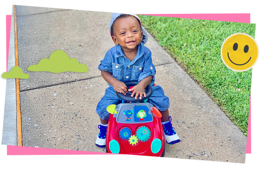 Child riding a Busy Buggy on a sidewalk, surrounded by cartoon clouds and a smiley face.